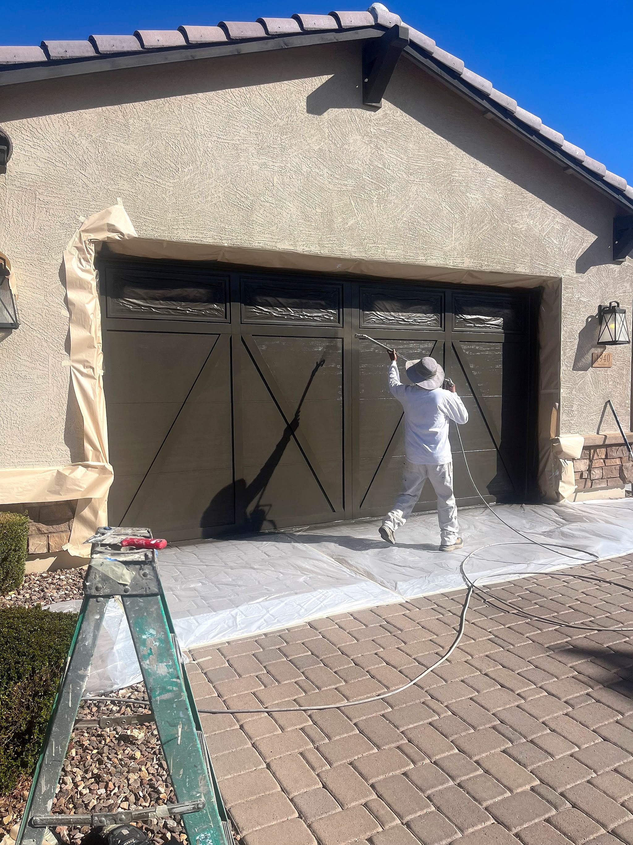 Painter in whites spraying a dark garage door, masking paper down