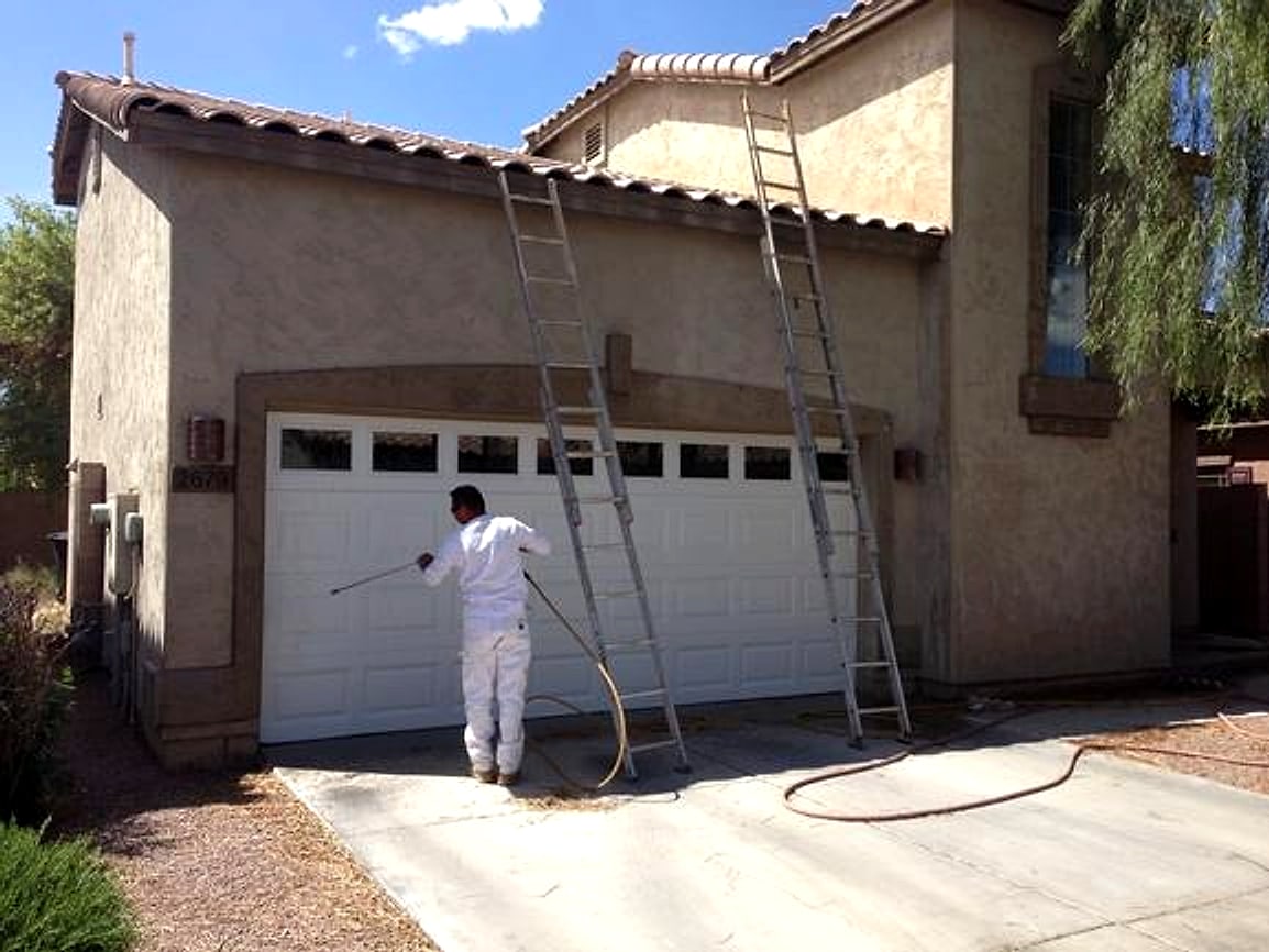 Painter spraying a garage door with ladders up