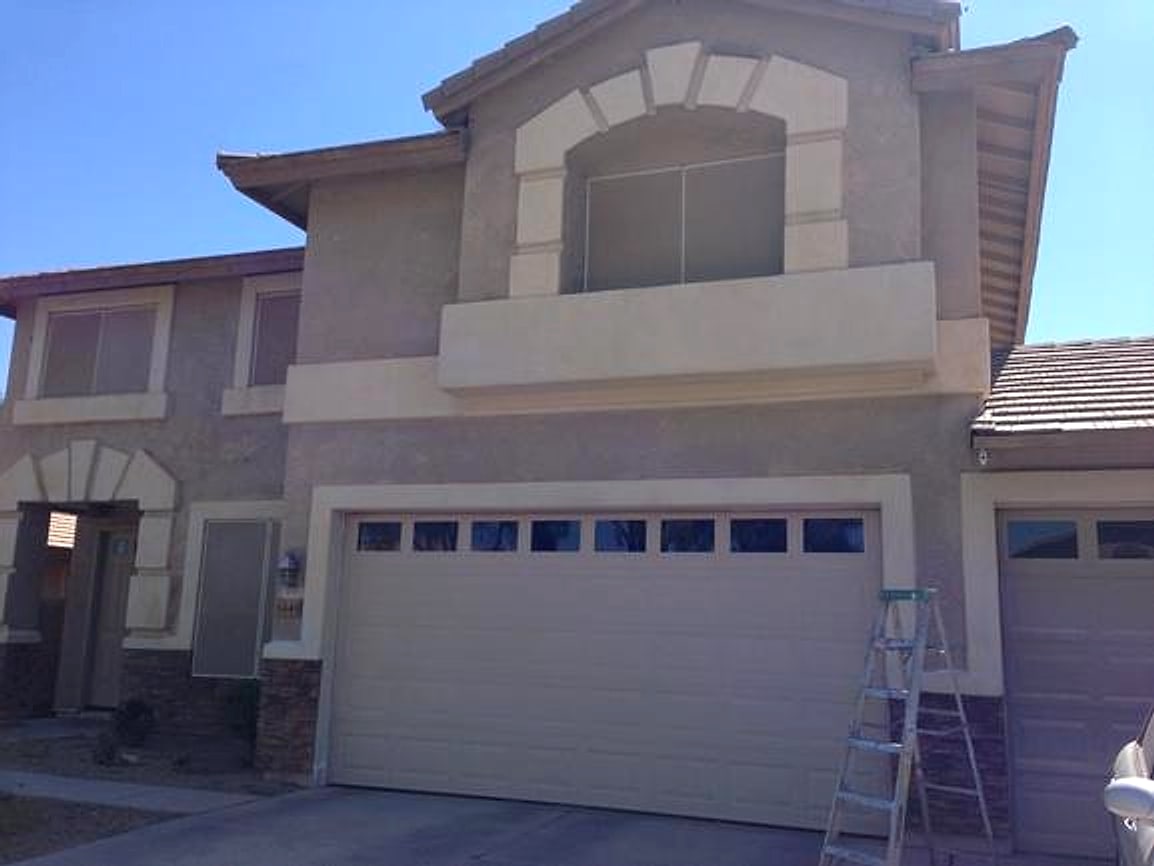 Two-story stucco home mid-job with a ladder up
